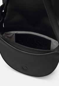 Sac bandoulière en cuir noir ouvert pour montrer la doublure intérieure lisse gris clair et une étiquette noire avec le nom de la marque embossé.