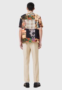 Camisa de manga corta de patchwork que presenta una mezcla de vibrantes patrones florales y abstractos, hecha de tela ligera y con un corte relajado.