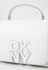 Fehér bőr kézitáska, amelyen a "DKNY" logó domború, strukturált kialakítással, felső fogantyúval és diszkrét varrási részletekkel rendelkezik. Puha tapintás kék díszítéssel.