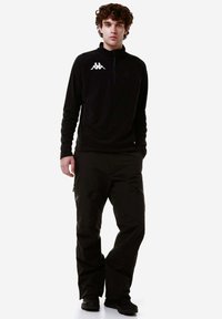 Pullover in pile nero con zip a quarto e logo bianco, abbinato a pantaloni impermeabili neri con diverse tasche con zip e una vestibilità comoda.