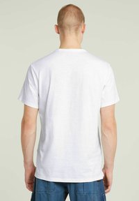 T-shirt bianco in cotone con maniche corte e scollatura rotonda, mostrato di spalle. Design semplice con una texture liscia.