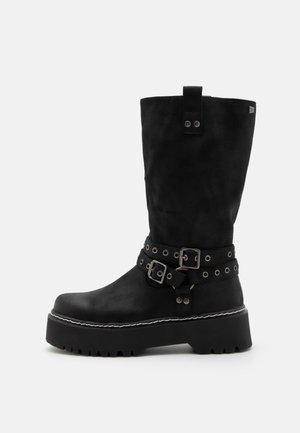 Mustad säärtesse ulatuvad saapad, mis on valmistatud seemisnahast, pakuvad paksu platvormitalda, pandlaaktsente ja dekoratiivset riistvara varrel.