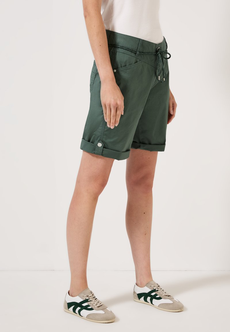 Donkergroene shorts met een relaxte pasvorm, een trekkoord in de taille, omgeslagen hems en zijzakken. Gepaard met witte en grijze sneakers.