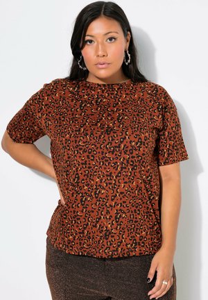 T-shirt corto marrone a maniche corte con stampa leopardata nera e oro, caratterizzato da un colletto rotondo e una vestibilità rilassata. Indossato con pantaloni scuri lucidi.