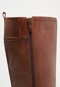 Stivale in pelle marrone con cerniera laterale, pannello elastico e dettagli di cucitura visibili; superficie liscia e strutturata.