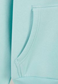 Lysblåt sweatshirtstof med ribstrikkede manchetter og en stor forlommer. Blød tekstur og minimal syning detalje.