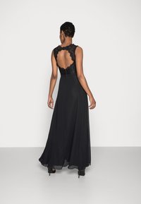 Svart formell klänning med en spetslivstycke med scallopad halsringning och öppen rygg, flödande kjol och klackskor. Mjuk textur.