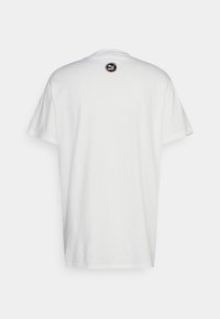 Bílá tričko vyrobené z bavlny, s kulatým výstřihem a krátkými rukávy. Logo Puma v černém kruhu na horní části zad. Hladká textura.
