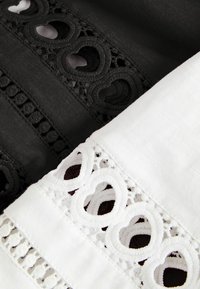 Tessuto in bianco e nero con ritagli in pizzo a forma di cuore e dettagli ricamati, sovrapposti diagonalmente l'uno sull'altro.