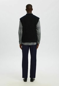 Tamsiai mėlynas ridų megztinis virš šviesiai pilkos languotos marškinės su mygtukais, derinamas su tamsiai mėlynomis kelnėmis. Lygus paviršius, prigludęs dizainas ir jokios matomos raštų.