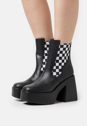 Svarta läderankelstövlar med tjock klack, utrustade med elastiska sidopaneler i schackrutigt mönster för flexibel passform och geometrisk design.