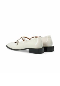 Scarpe in pelle verniciata bianca con punta affusolata, tacco blocco nero basso e cinturino regolabile intorno al metatarso, con un fiocco decorativo.