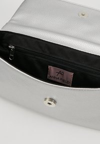 Silver leather clutch bag with a textured surface. The interior is black with a zip pocket. Features a magnetic snap closure and a brand label.