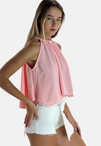 Top rosa claro de halter con diseño plisado, que presenta un frente drapeado y lados abiertos. Combinado con pantalones cortos blancos con dobladillo deshilachado.