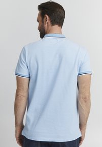 Svetlobluz t-shirt s kratkimi rokavi iz mehkega materiala, s klasičnim ovratnikom, kratkimi rokavi z temno modrim robom in ravnim robom.