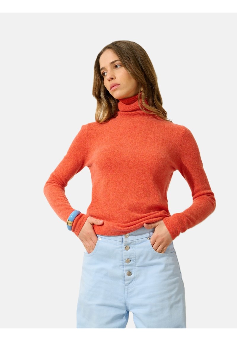 Roter Rollkragenpullover aus weichem, strukturiertem Material, figurbetontes Design mit langen Ärmeln, kombiniert mit hellblauen Jeans mit hoher Taille.