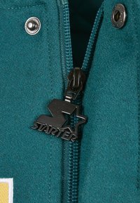 Tee groene fleece met een zwarte ritsen trekker met het woord "STARTER" en een sterlogo. Metaal drukknoophardware zichtbaar.