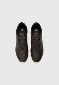 Bruna lädersneakers med slät yta, perforerade sidor, platta snören och rundad tå, med gummisulor och subtil branding.