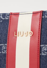 Jeanstasche mit roten und weißen gestreiften Lederakzenten. Prominent sichtbares goldenes Logo "LIU·JO". Kontrast zwischen strukturiertem Stoff und glattem Leder.