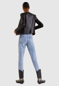 Černá kožená zkrácená bunda, vybledlé modré úzké džíny a dekorativní černé kovbojské boty s bílými akcenty. Model je viděn zezadu.