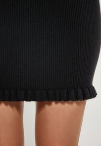 Fustă din tricot negru cu dantelă la margine. Textura este netedă, iar designul este mulat, evidențiind silueta.