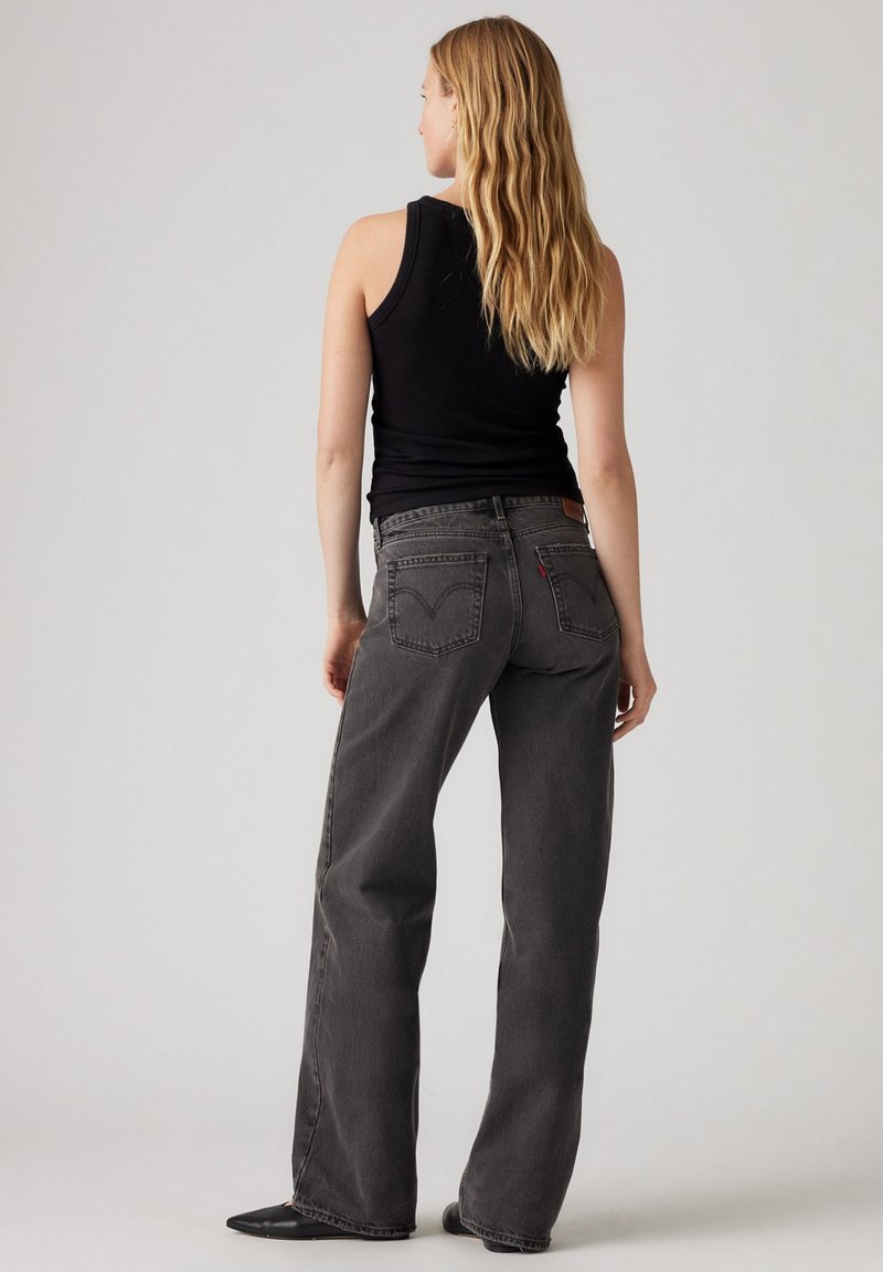 Top negro sin mangas combinado con jeans de mezclilla de pierna ancha y tiro alto en un gris antracita desvaído. Características notables incluyen bolsillos traseros y un parche con el logotipo.