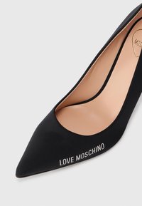 Pantofii cu toc ascuțit negri, confecționați dintr-un material fin, având o branț nude și textul argintiu "LOVE MOSCHINO" pe lateral. Design minimalist, formă elegantă.