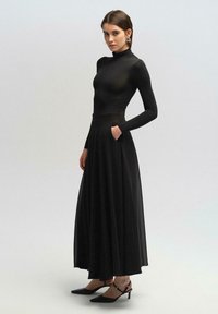 Vestido negro con un corsé ajustado de manga larga y una falda fluida hasta los tobillos. Cuenta con bolsillos laterales y una textura suave y translúcida.