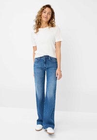 Blauwe flared jeans met een lichte wassing en een lichte vervaging, gecombineerd met een wit T-shirt met korte mouwen en witte sneakers.
