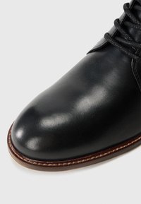 Zapato de cuero negro con un acabado suave y brillante. Punta redonda, diseño de cordones y costuras en contraste a lo largo de la suela.