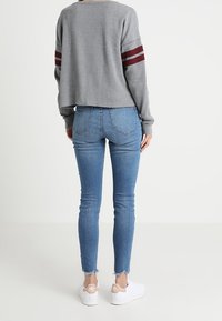 Szary krótki sweter z bordowymi paskami, zestawiony z dopasowanymi niebieskimi dżinsami z postrzępionymi brzegami oraz białymi trampkami z brązowymi akcentami.