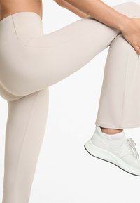 Beiga leggings med en slät textur, hög midja och en åtsittande siluett, kombinerat med ljusa sportskor.