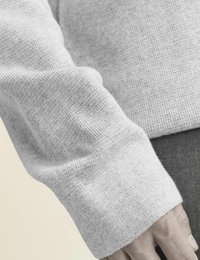 Grau gestrickter Pullover mit einer strukturierten Oberfläche. Er hat einen breiten Bund und eine leicht lockere Passform. Das Material wirkt weich und leicht.