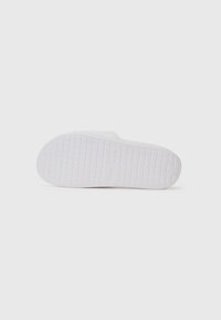 Semelle en caoutchouc blanc avec une surface texturée à motif en grille et un détail logo central. Aucune marque ou usure visible.