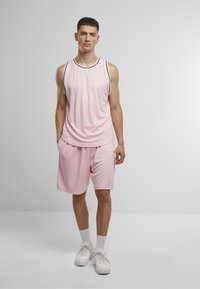 Lyserød atletisk tanktop med sort trim, parret med matchende lyserøde shorts. Letvægtsstof, afslappet pasform, og hvide sneakers fuldender looket.