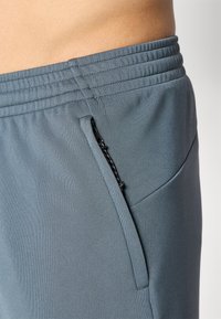 Grijze sportshorts met een gladde textuur, voorzien van een ritszak en een elastische tailleband met gathered details.