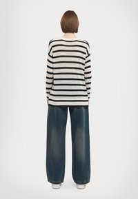 Pull rayé en crème et noir, coupe ample, avec un col rond et des manches longues. Associé à un pantalon en denim bleu à pattes larges.