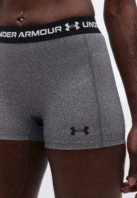 Κοντινό πλάνο ατόμου που φοράει γκρι συμπιεστικά σορτς Under Armour με το λογότυπο της μάρκας στη μέση και στον μηρό, εμφανίζοντας τατουάζ στο χέρι και τρύπα στον αφαλό.