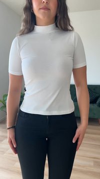 Top bianco a maniche corte con collo alto, dalla texture liscia e design aderente, abbinato a pantaloni neri con cerniera e tasche.