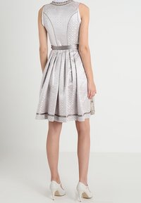 Robe gris clair avec jupe plissée, tissu texturé, ceinture en satin et haut à motif. Paire de chaussures blanches à talons hauts visible.