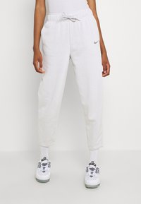 Ljusgrå sweatpants med elastiskt midjeband och dragsko, med en liten Nike-logotyp. Tyget är mjukt och slätt med en avslappnad passform.