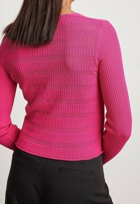 Eng anliegender, rosa gerippter Pullover mit strukturierten Streifen, langen Ärmeln und rundem Ausschnitt, kombiniert mit schwarzer Hose.