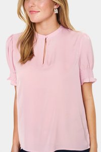 Pink short-sleeve blouse in lightweight fabric with a keyhole neck opening, smocked detailing on sleeves, and a relaxed fit.