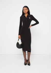 Fekete, hosszú ujjú, testhezálló ruha galléros nyakkivágással és gombdíszítéssel. A mellrészen gyémánt hímzés található, hossza midi.