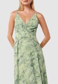 Green marbled maxi dress with a plunging V-neck, thin straps, gathered bust detail, and textured fabric, featuring ruffled accents along seams.