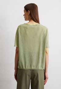 Light green, short-sleeved sweater with a loose fit and a textured finish. Rounded neckline and dropped shoulder seams, paired with olive pants.
