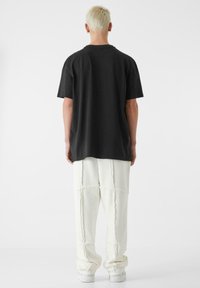Črna t-maica sproščene silhuete s kratkimi rokavi, v kombinaciji z belimi širokimi hlačami z vidnimi šivi in mehkimi tkaninami.