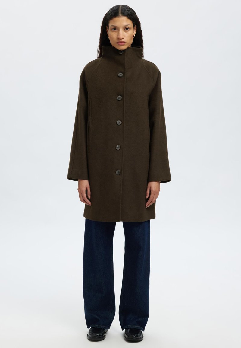 Manteau brun, longueur genou, avec un col haut, six boutons sur le devant et des poches latérales. Le tissu semble doux et texturé.