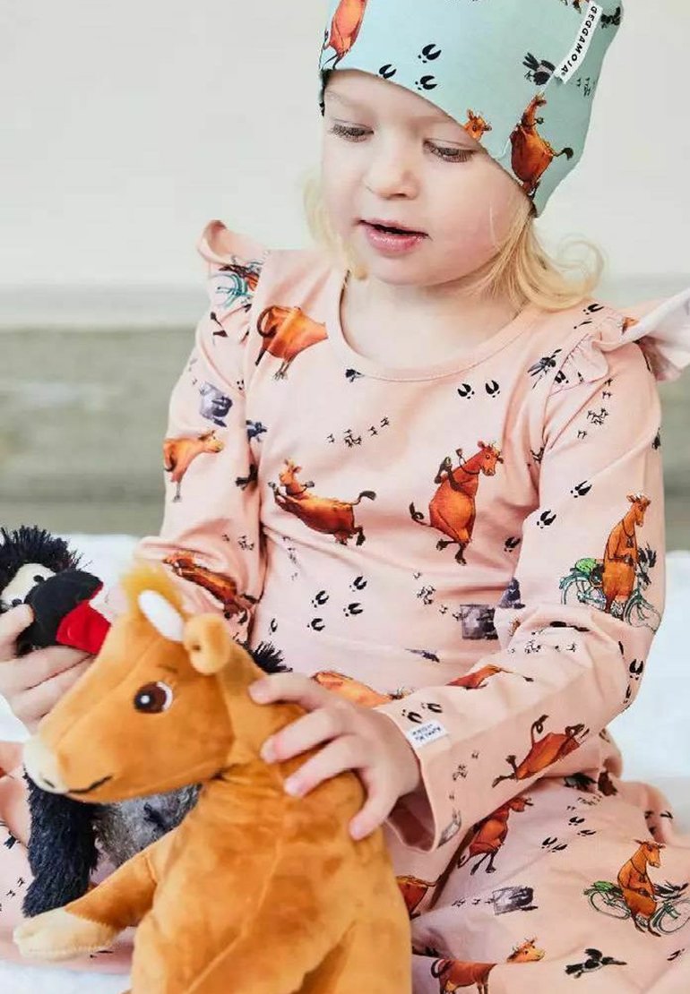 Pitkähihainen vaaleanpunainen pyjamapaita eläinkuvioilla, röyhelöhihnat ja samaa sävyä oleva vaaleansininen hattu. Lapsi pitää sylissään pehmoleluja: lehmää ja pingviiniä.