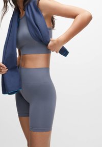 Un crop top de sport gris et un short taille haute, en tissu extensible, accompagnés d'une serviette rayée bleue portée sur les épaules.